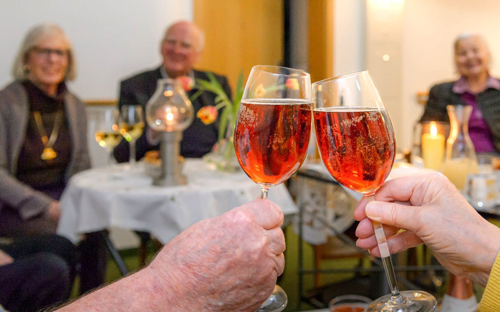 Anstoßende Sektgläser; Senior*innen unscharf im Hintergrund