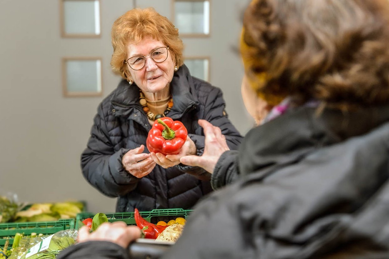  Barbara Wrage reicht der Verkäuferin eines Gemüsestandes eine rote Paprika  