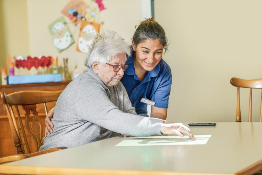 Eine Mitarbeiterin und eine Bewohnerin der Tagespflege spielen ein Spiel, welches auf den Tisch projiziert wird
