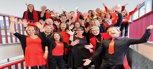 Cruise of Music Rot-schwarz gekleidete Chormitglieder stehen lächelnd und posierend auf einer Treppe.