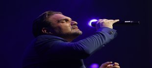 Singender Mann mit drei Tage Bart, vor einem blauen Scheinwerfer