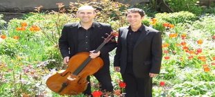 Zwei Musiker in schwarzer, eleganter Kleidung stehen in einem blühenden Garten zwischen roten Tulpen. Eine Person hält ein Cello, beide präsentieren sich in ruhiger, gepflegter Umgebung im Freien.
