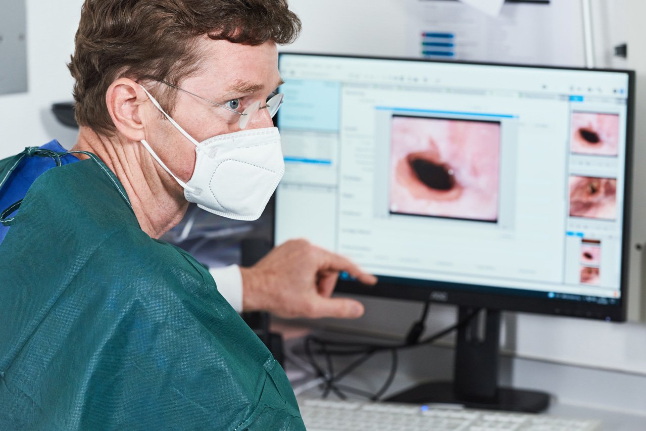 Ein Arzt sitzt vor einem Monitor mit endoskopischen Aufnahmen und erläutert das GEzeigte.