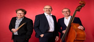 Die Musiker des Frank Muschalle Trio vor rotem Hintergrund