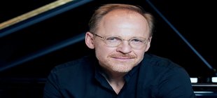 Schwarzgekleideter Mann mit Brille vor einem Konzertflügel