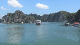 Wasserfläche mit Booten, Häusern am Ufer und mit Bergen im Hintergrund