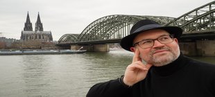 Porträt Björn Heuser vor dem köln-Panorama