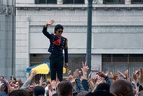 Michael Jackson steht erhöht inmitten einer Menschenmenge mit ihm zuwinkenden Händen.