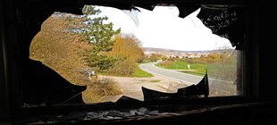 Blick durch ein zerbrochenes geschwärztes Fenster auf eine Landschaft