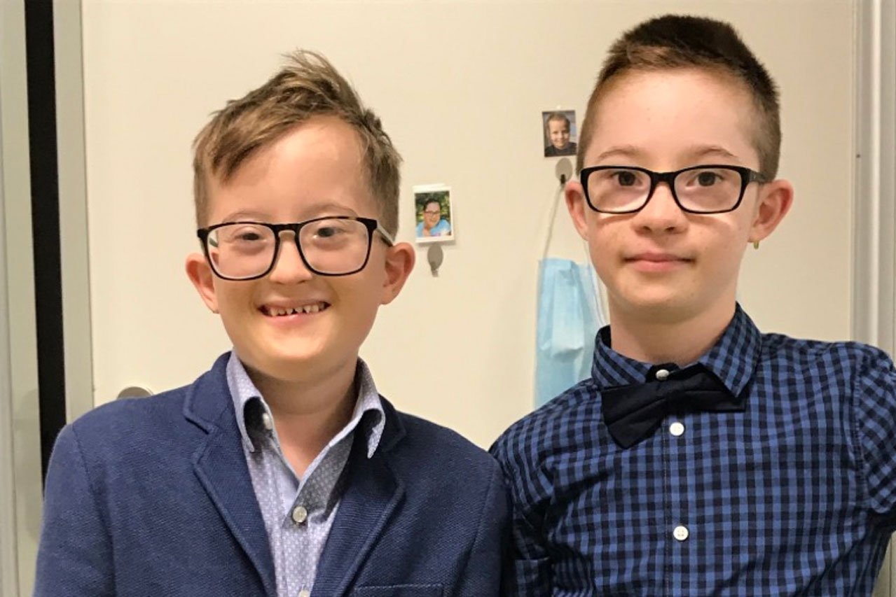 Zwei Jungs schauen in die Kamera, einer lacht. Sie tragen beide ein Hemd und eine Brille