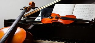 Eine Geige liegt auf einem aufgeklappten schwarzen Flügel, ein Cello lehnt daran.