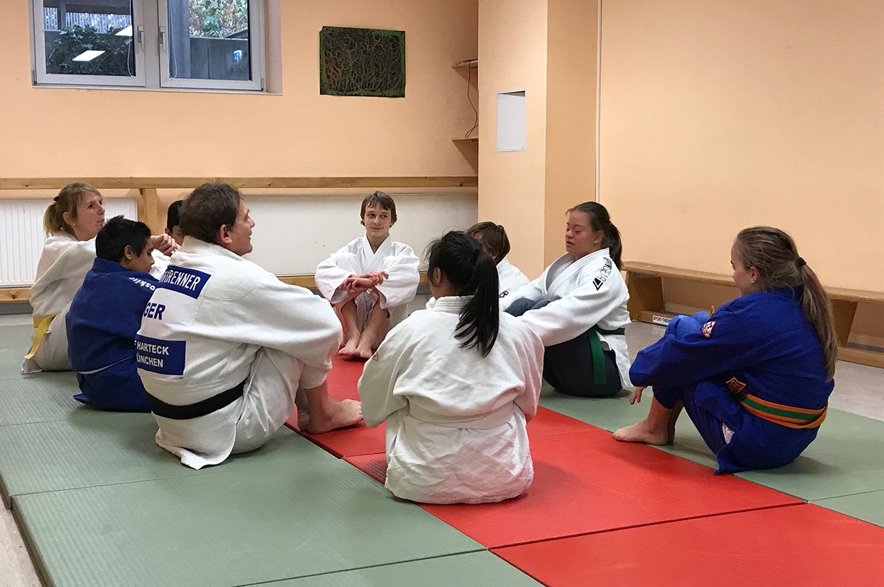 Judoka in typischer Sportkleidung sitzen im Kreis