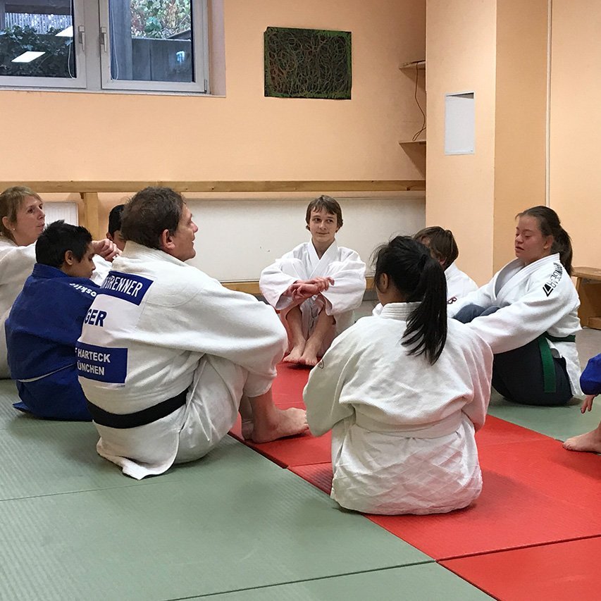 Judoka in typischer Sportkleidung sitzen im Kreis