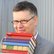 Mann mit Brille und einem Bücherstapel vor einer grauen Wand
