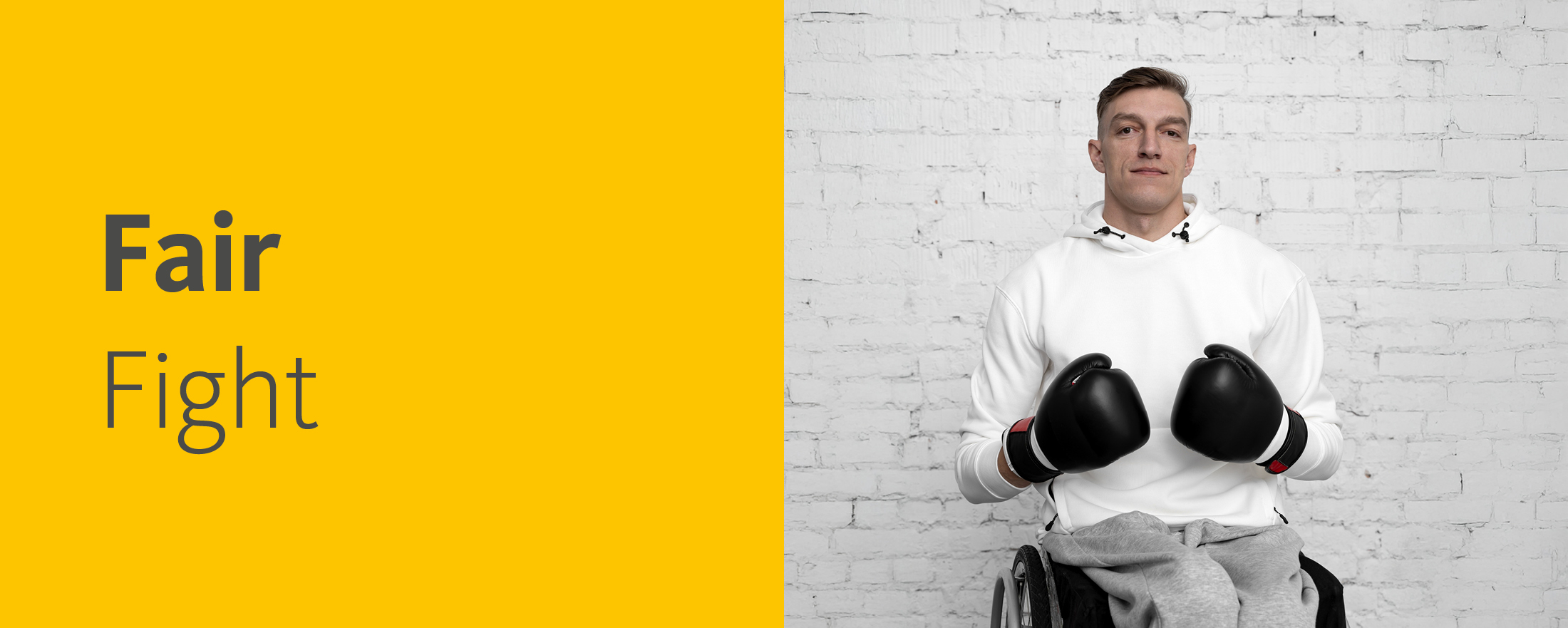 Ein junger Mann sitzt im Rollstuhl und hält die Hände mit schwarzen Boxhandschuhen angriffslustig vor sich